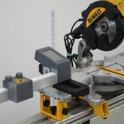 Butée numérique pour scie Pedante installée à gauche d’une scie à onglet DeWALT sur un piétement mobile DeWALT DE7023-XJ.