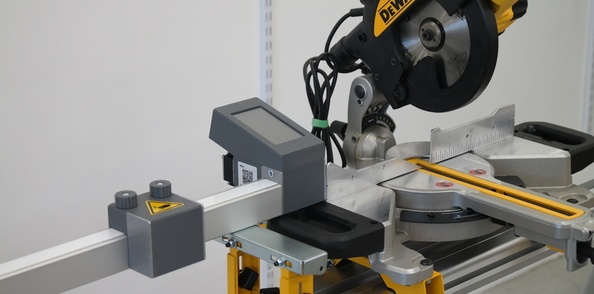 Butée numérique pour scie Pedante installée à gauche d’une scie à onglet DeWALT sur un piétement mobile DeWALT DE7023-XJ.