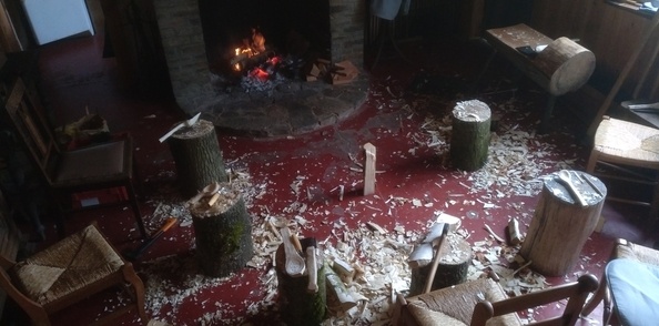 Des bouts de bois vert, des billots, des haches et des couteaux de sculpture au coin du feu ouvert.